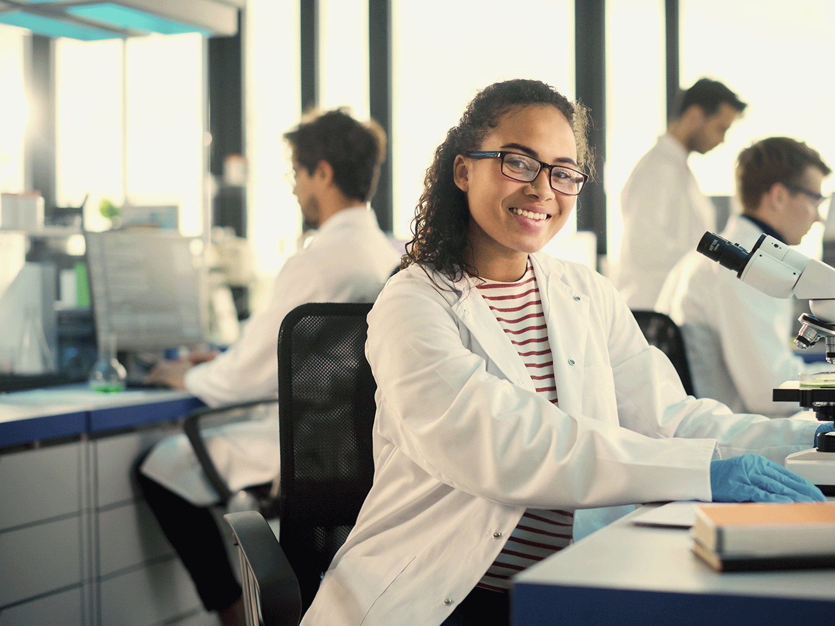 A woman in a biology major program sits in a classroom in front of a microscope.
