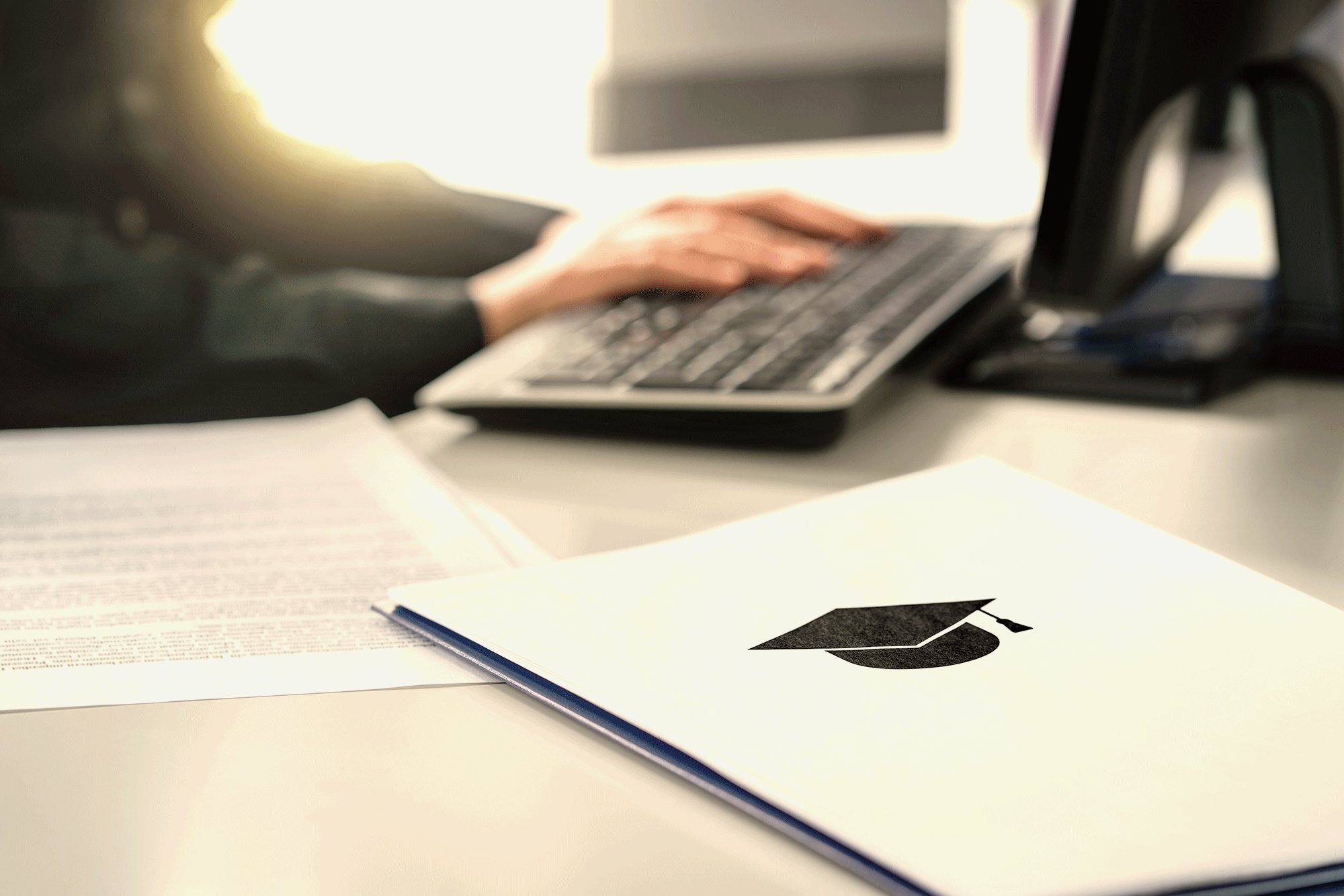 A person types on a computer keyboard with folders indicating a college application nearby.