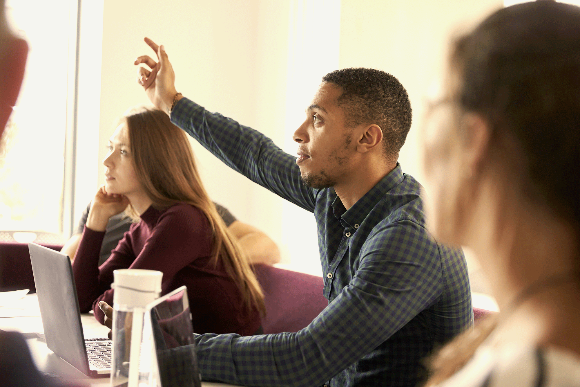 A student raises his hand in class as he engages with college coursework.