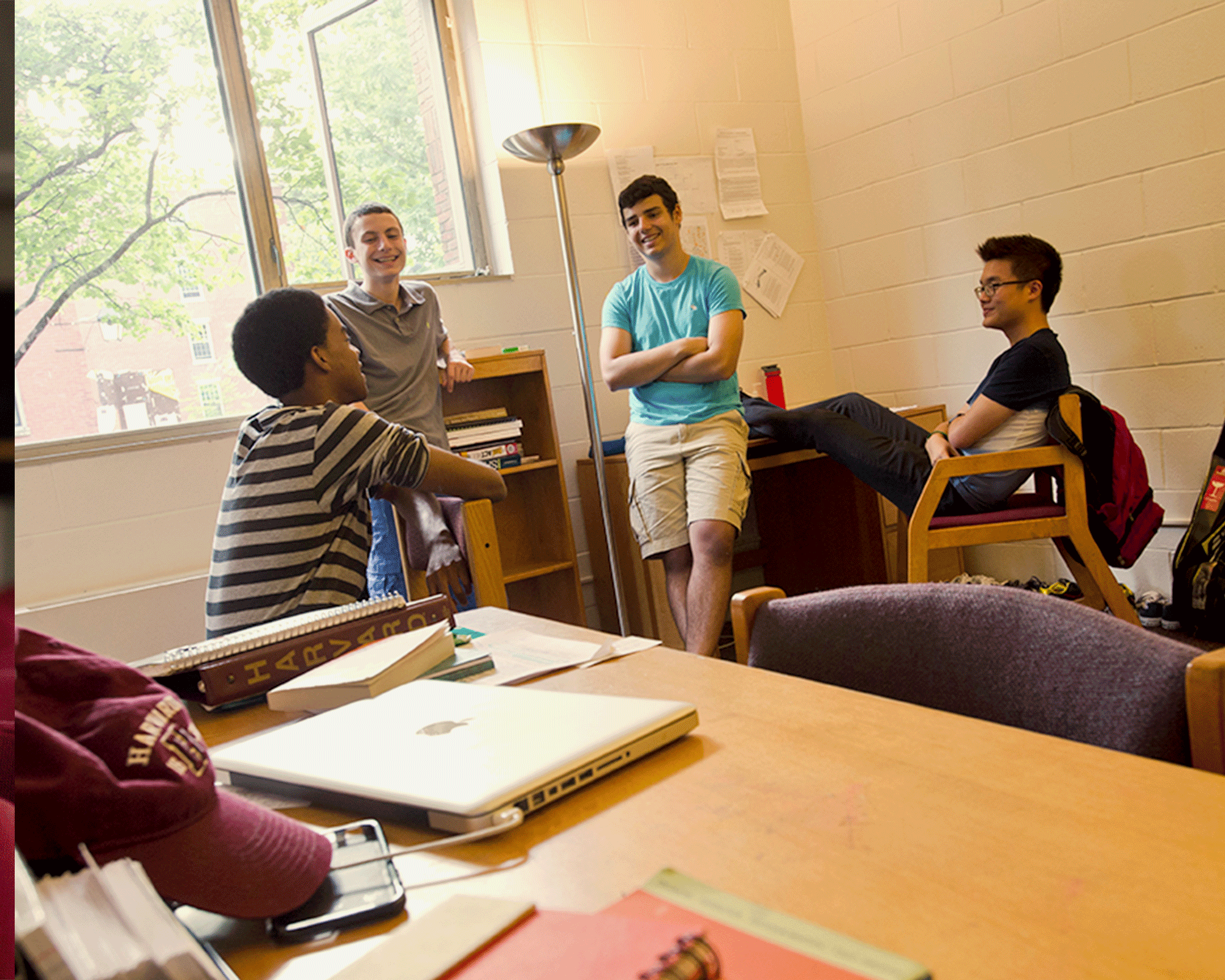 Four high school students stand around talking in a college dorm room.