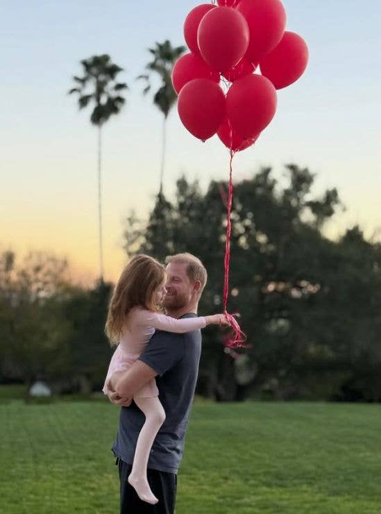 Prince Harry carrying Princess Lilibet, who holds a bunch of balloons