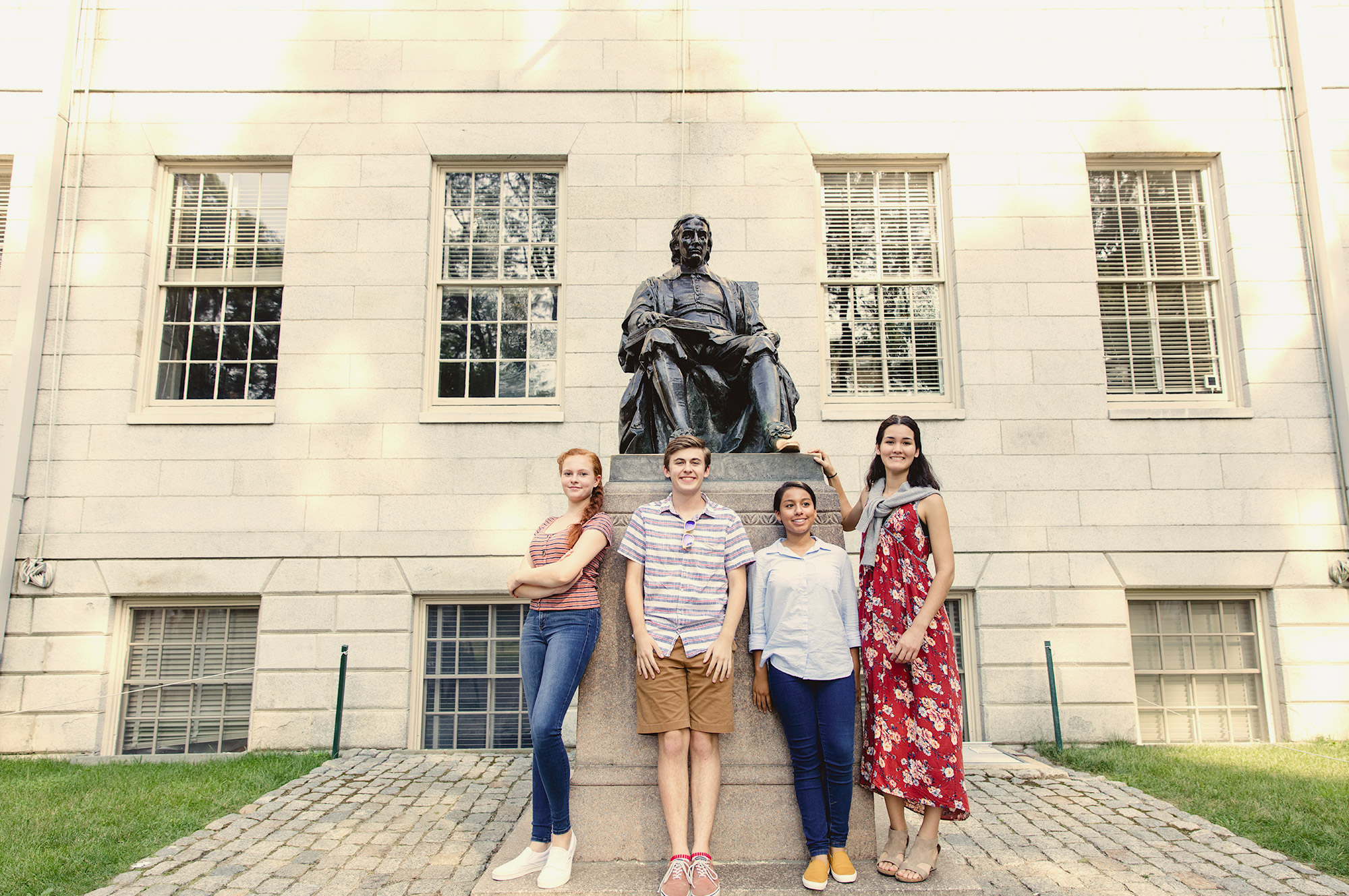 4 students standing in front of John Harvard statue in Harvard Yard.