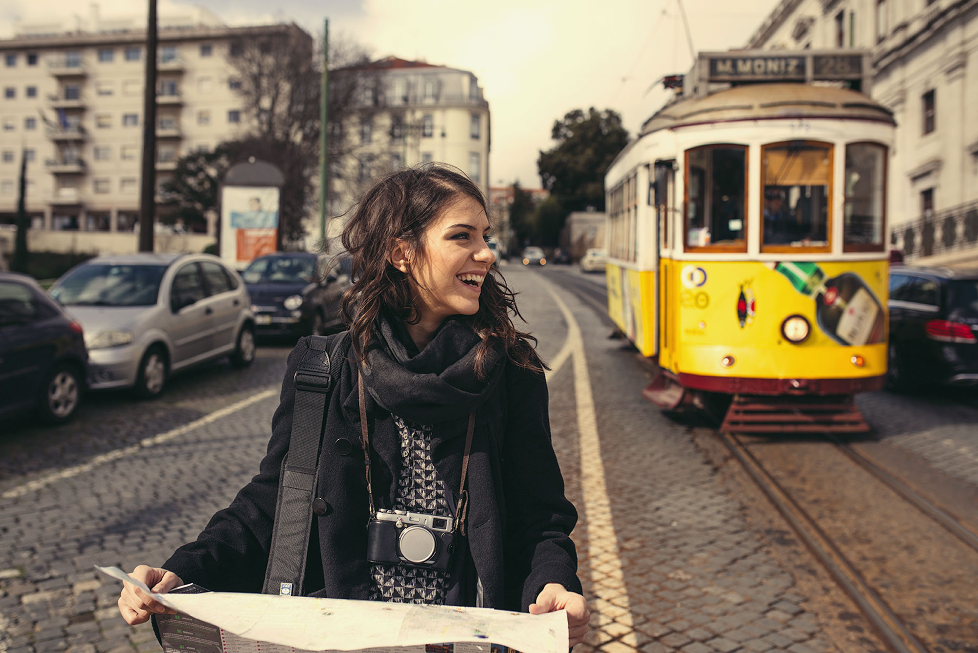 A smiling female student holds a map while walking down the street in Lisbon, Portugal.